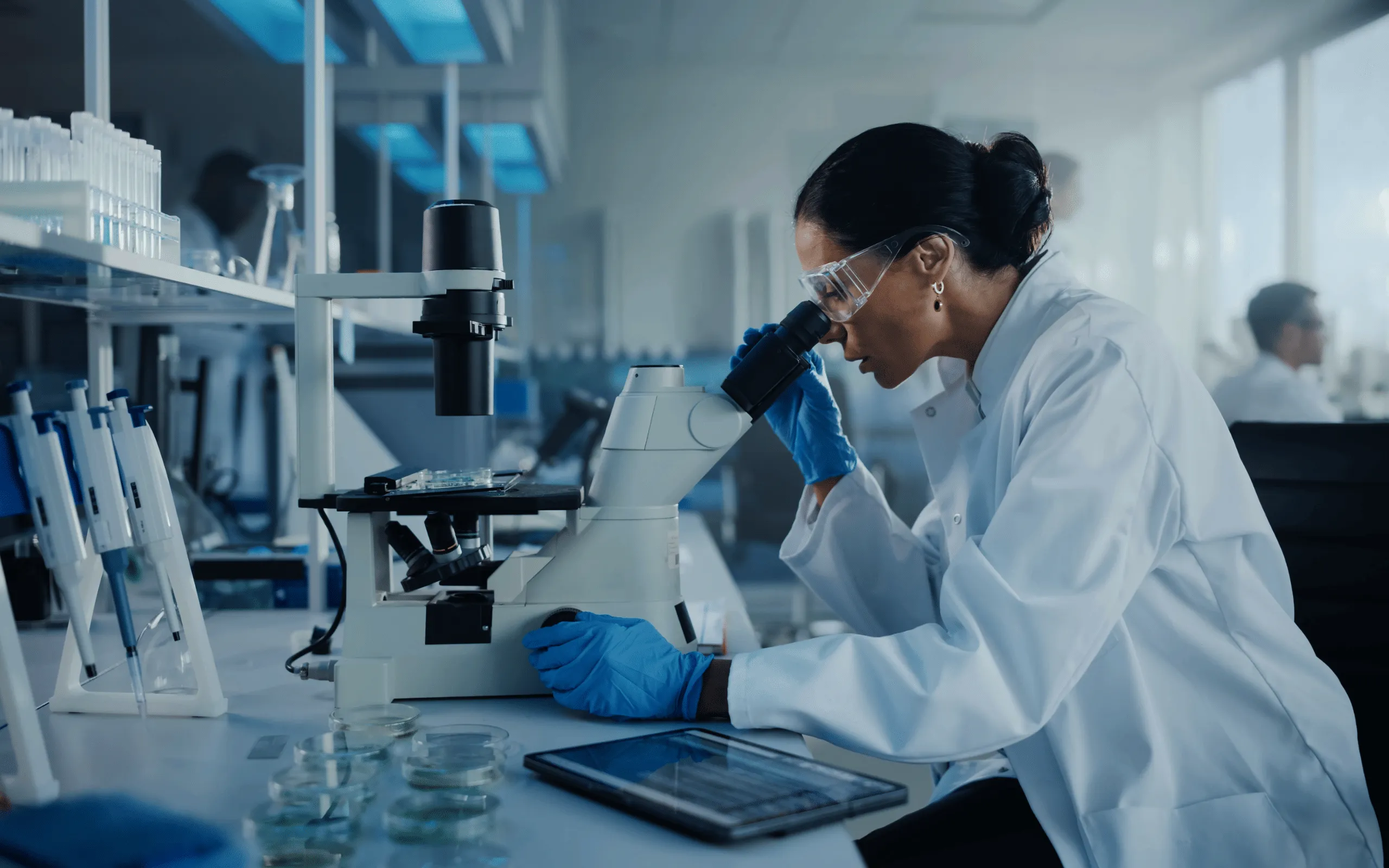 A Mohs technician, in a lab coat, examines a sample using a microscope in a dimly lit laboratory.